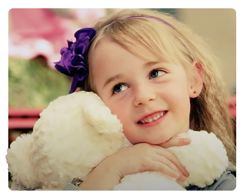 Small smiling girl cuddling a white plush toy teddy bear