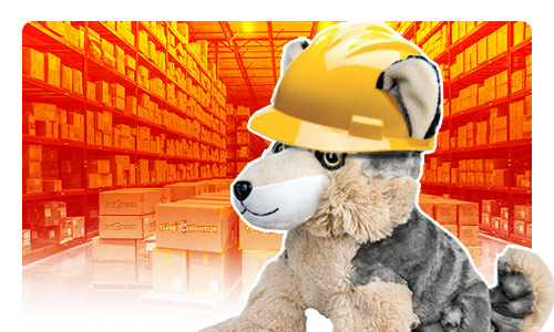 Plush toy wolf wearing a yellow helmet with warehouse in the background